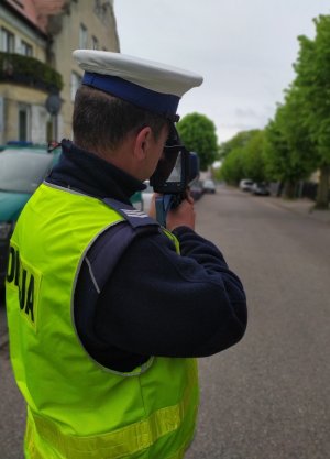 Policjant stojący tyłem, trzymający w rękach laserowy miernik prędkości