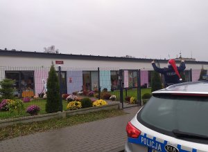 Policjant w czapce Mikołaja macha do dzieci przed przedszkolem