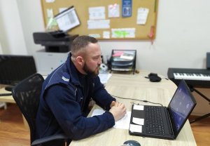 policjant przeprowadzający zajęcia on-line z młodzieżą, siedzący przed laptopem