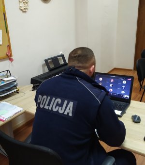 na zdjęciu znajduje się policjant siedzący twarzą do laptopa. Widać plecy z napisem &quot;POLICJA&quot;