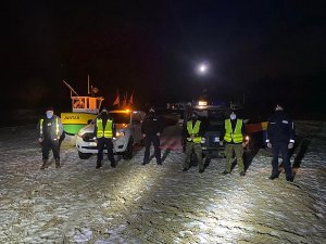 Policjanci wspólnie z funkcjonariuszami Urzędu Morskiego i Straży Granicznej, stojący w odstępach na plaży nocą